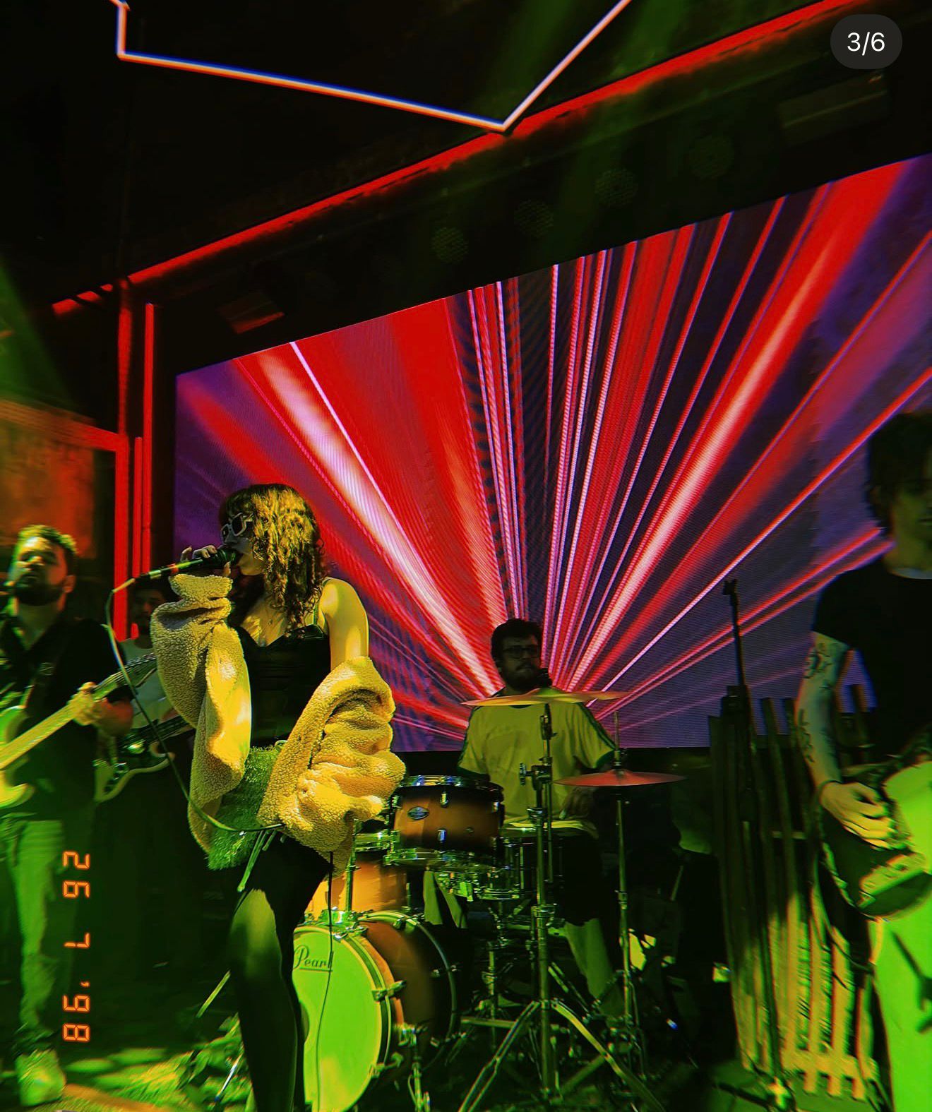 Binova e sua banda no palco diante de um painel de LED vermelho