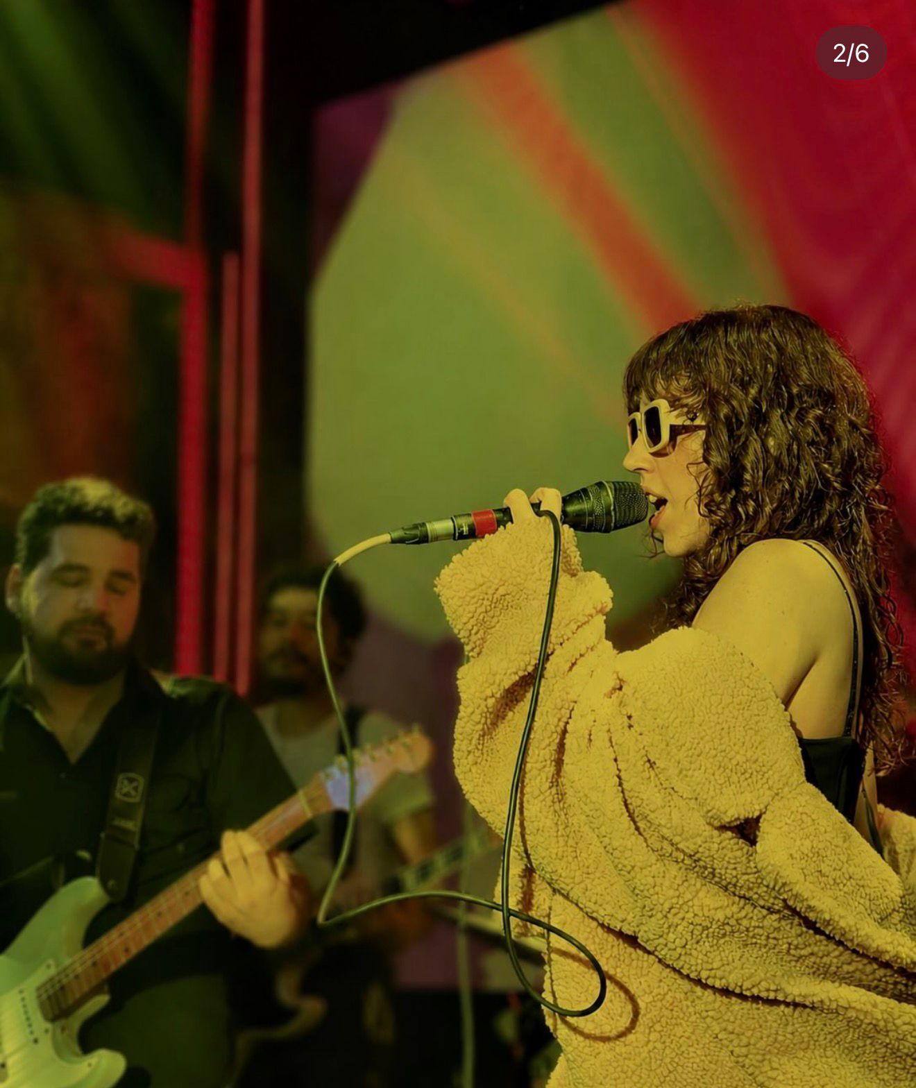 Binova cantando ao microfone com casaco felpudo no palco